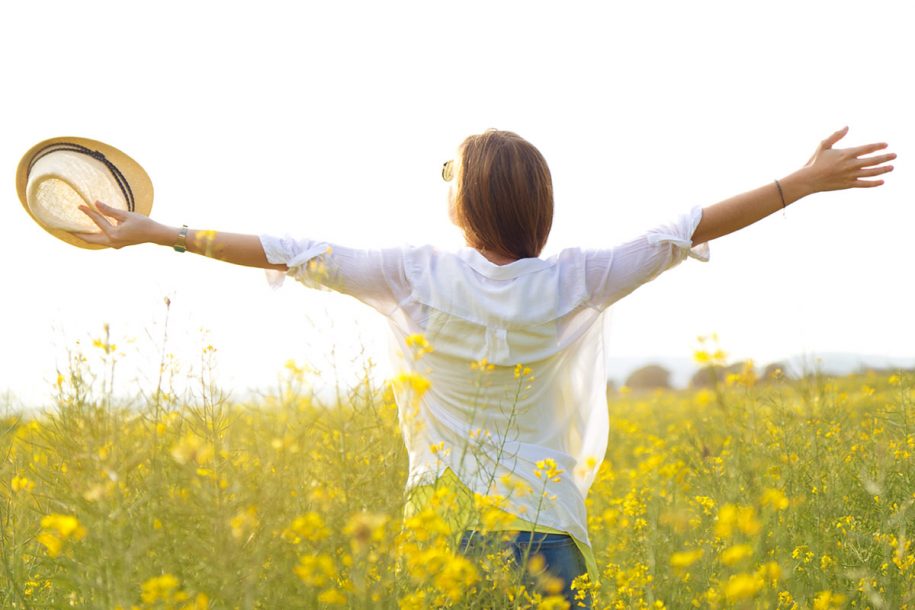 Woman among yellow flowers opening her arms in the sun